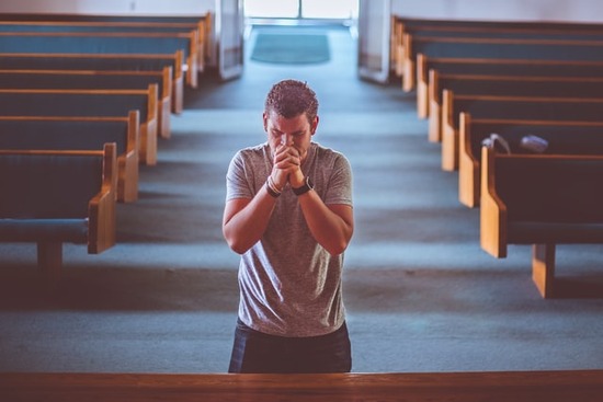 A man folding his hands and bowing his head at the front of a church.