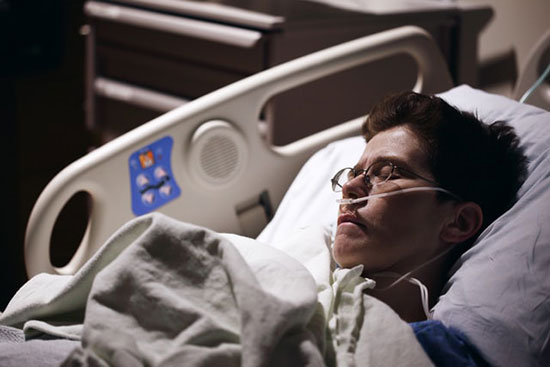 An ill man lies asleep in a hospital bed.