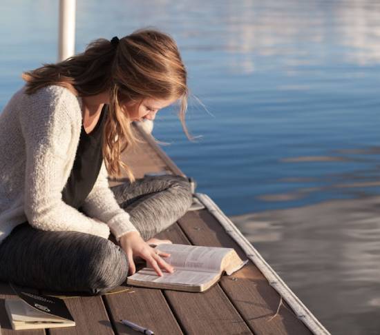 Woman sitting at the shore of a lake, daily feeding on the Word of God, the Bible